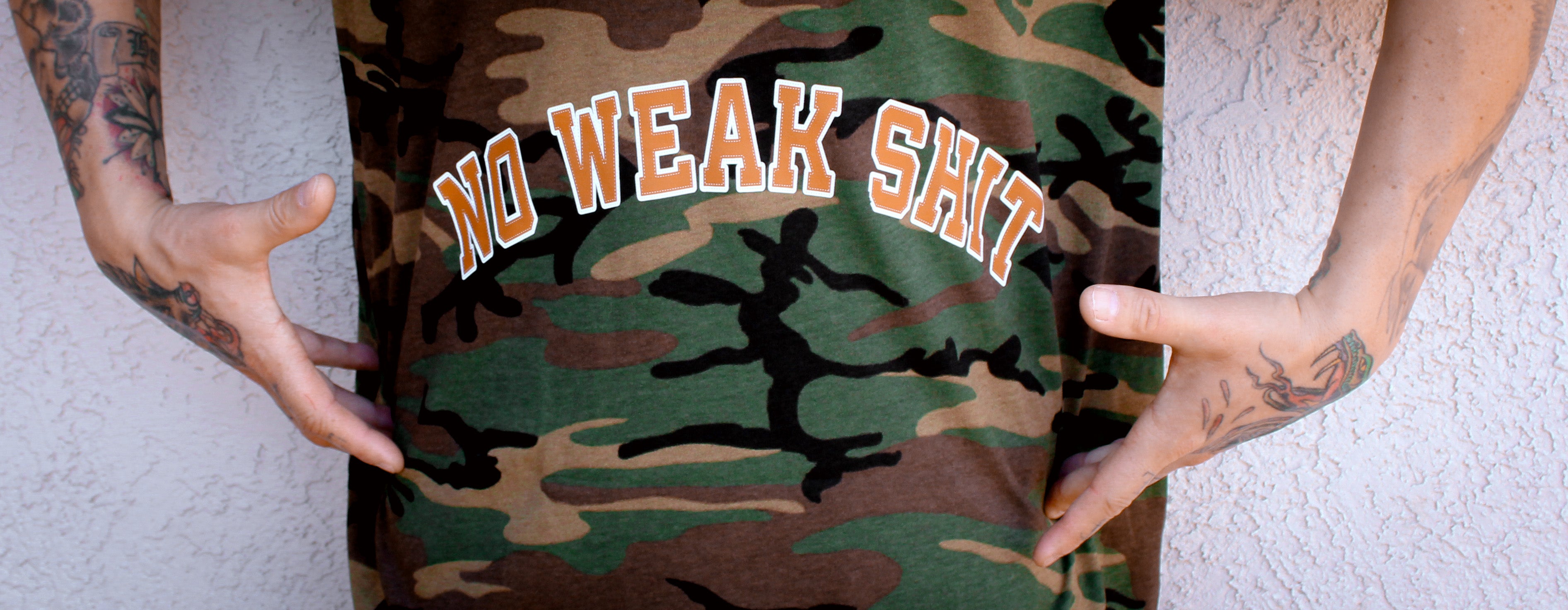 Camouflage t-shirt with 'NO WEAK SHIT' text held by a person.